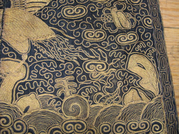 Raised gold embroidery forms intricate scrollwork and animal motifs on a dark textile over wood flooring.