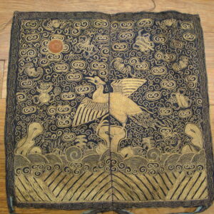 Ornate dark blue and gold square textile with a flying bird pattern rests on a brown hardwood floor.