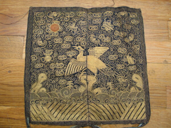 Ornate dark blue and gold square textile with a flying bird pattern rests on a brown hardwood floor.