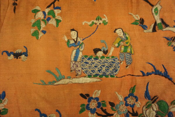 Highly textured orange rug featuring intricate embroidery of two figures and blue and white geometric forms.