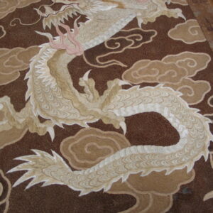 Textured rug detail with a coiled beige dragon and pink claws set against a dark brown field with tan clouds.