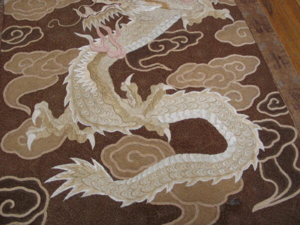 Textured rug detail with a coiled beige dragon and pink claws set against a dark brown field with tan clouds.