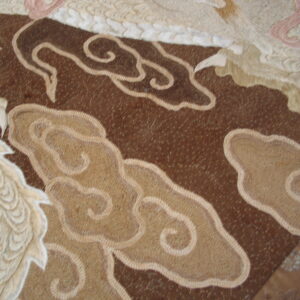 Textured brown and tan rug detail showing raised cloud motifs and dimensional white feathered patterns with pink accents.