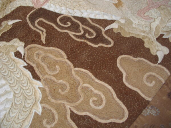 Textured brown and tan rug detail showing raised cloud motifs and dimensional white feathered patterns with pink accents.