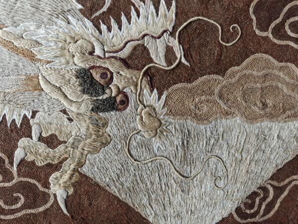 Detail of a brown rug showing a shaggy beige dragon head and claws surrounded by low-pile woven clouds.
