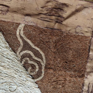 Close detail of a brown looped rug with light curved patterns adjacent to a section of long, shaggy beige pile.
