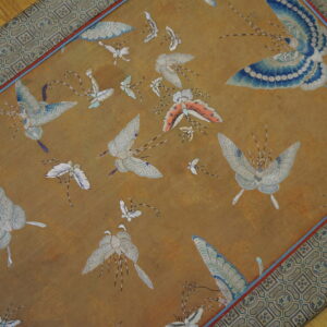 Detailed gold rug with scattered blue, white, and orange butterfly designs and a wide geometric border.
