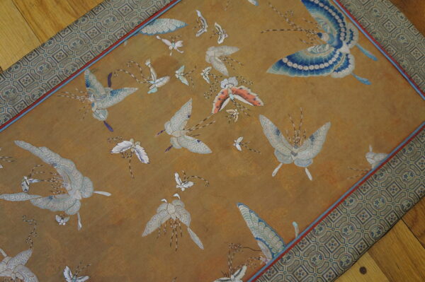 Detailed gold rug with scattered blue, white, and orange butterfly designs and a wide geometric border.