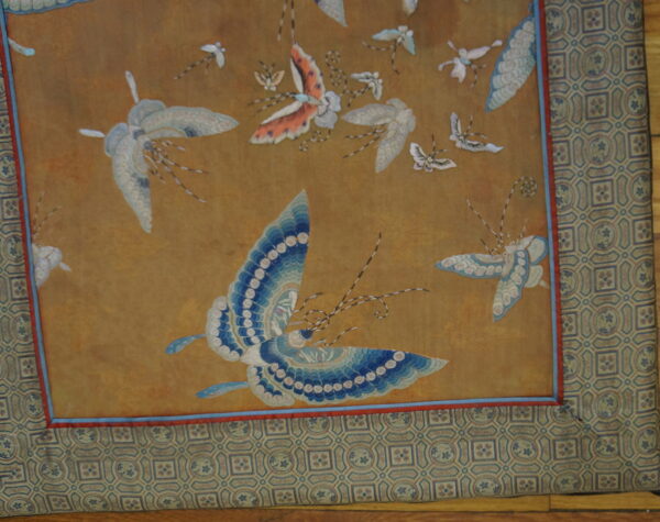 Gold field rug with blue and white insect motifs, surrounded by a complex geometric tile border.