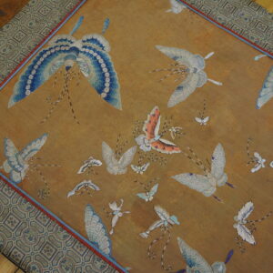 A gold-toned rug features detailed blue and white embroidered butterflies surrounded by a geometric patterned border.