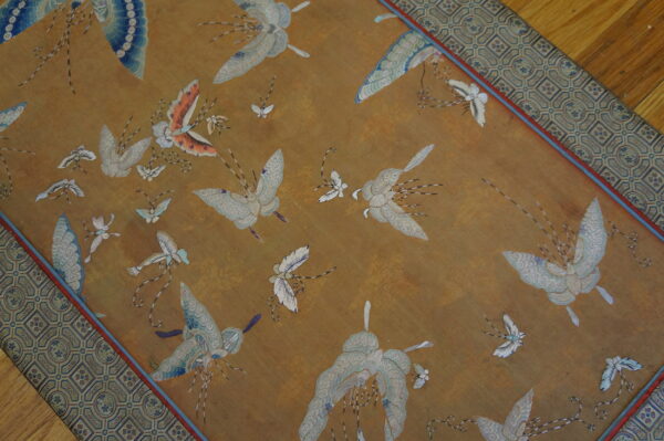 Gold runner rug with an overall pattern of white and blue flying insects and a geometric border on a wood floor.
