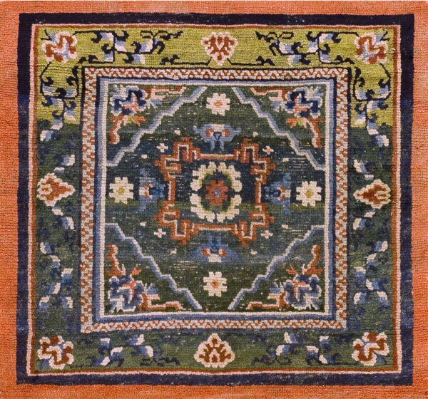 Square rug with a wide terracotta border framing complex geometric patterns in green, navy, and rust.