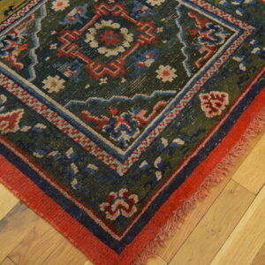 Geometric rug with deep green, red, and blue accents sits angled on light hardwood flooring.
