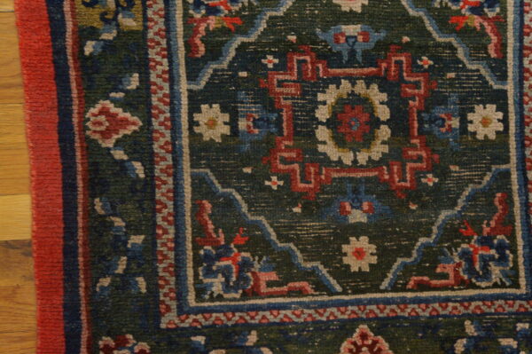 Corner of a multi-colored rug featuring geometric patterns in red, blue, and cream on a dark green field.