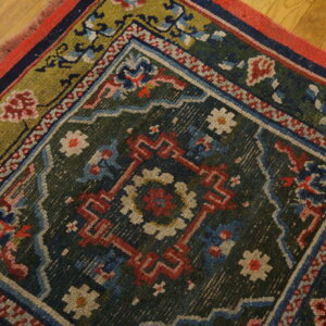 Dark green rug with red, blue, and olive geometric floral patterns lying on light hardwood flooring.
