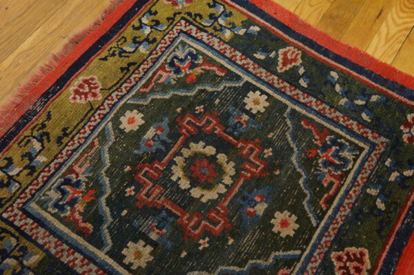 Dark green rug with red, blue, and olive geometric floral patterns lying on light hardwood flooring.