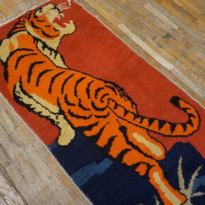 Rust-colored rug with an orange tiger motif and navy elements placed on gray plank flooring.