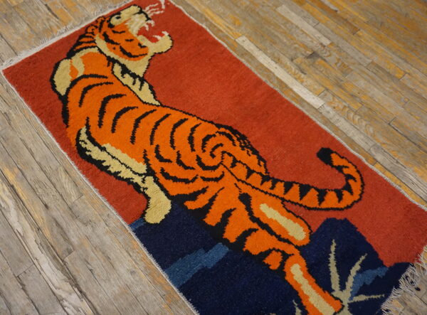 Rust-colored rug with an orange tiger motif and navy elements placed on gray plank flooring.