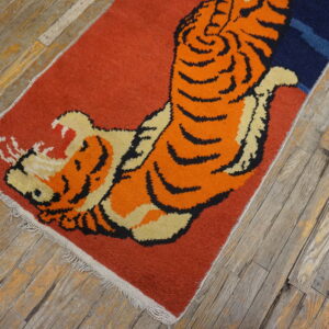 A rust-colored rug with a large orange, black, and cream roaring tiger motif on weathered wood flooring.