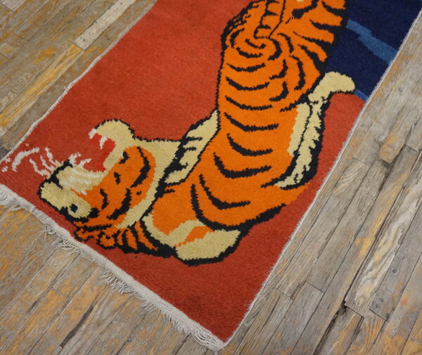 A rust-colored rug with a large orange, black, and cream roaring tiger motif on weathered wood flooring.