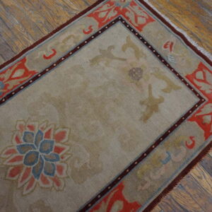 Low-pile taupe rug featuring floral designs in coral, blue, and brown rests on distressed wood flooring.