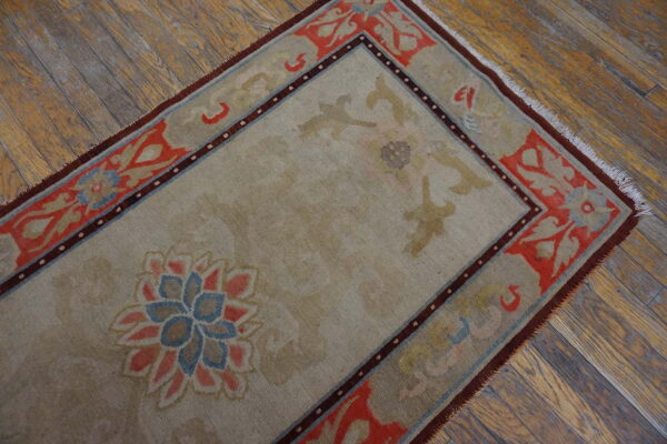 Low-pile taupe rug featuring floral designs in coral, blue, and brown rests on distressed wood flooring.