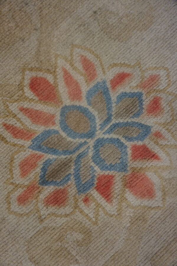 Textured rug close-up displaying a coral and blue stylized floral pattern against a neutral tan ground.