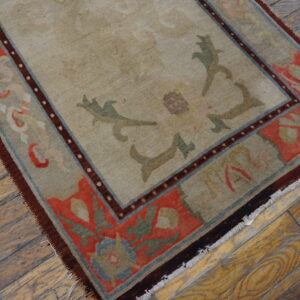 Beige rug with a complex coral and blue floral border displayed on worn hardwood planks.