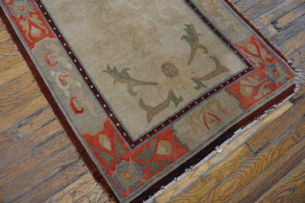 Beige rug with a complex coral and blue floral border displayed on worn hardwood planks.