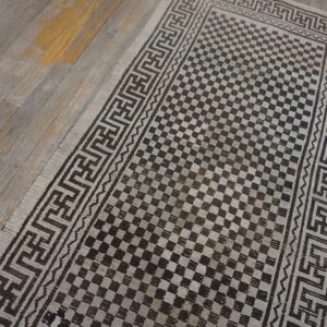 Dark brown and light beige runner featuring a checkerboard field and geometric key borders on wood flooring.