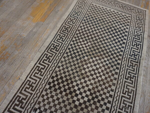 Dark brown and light beige runner featuring a checkerboard field and geometric key borders on wood flooring.