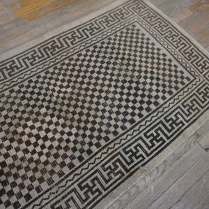 Dark brown and tan runner rug featuring a checkerboard pattern and geometric border on distressed gray wood.