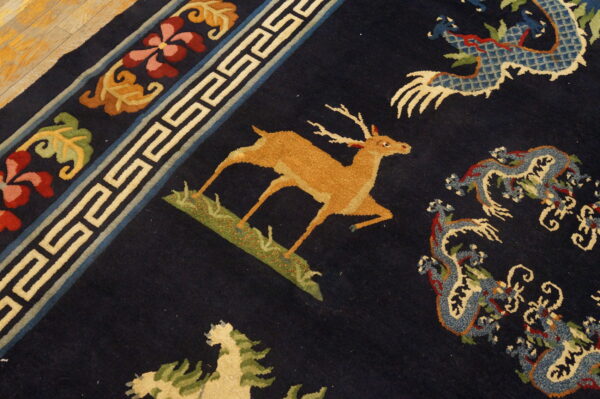 Detail of a blue rug showing a tan deer, patterned dragons, and a geometric and floral border on wood flooring.