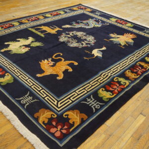 Square dark blue rug with multicolored mythical animal patterns and a geometric border on yellow wood planks.