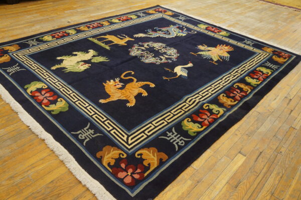 Square dark blue rug with multicolored mythical animal patterns and a geometric border on yellow wood planks.