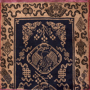 Tan and navy patterned rug featuring a central bird design and bordered by a wide strip of pleated magenta fabric.
