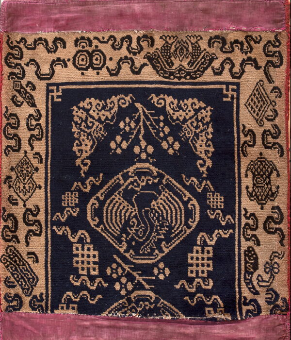 Tan and navy patterned rug featuring a central bird design and bordered by a wide strip of pleated magenta fabric.