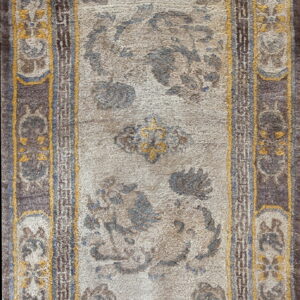 Plush rug with a thick brown border and abstract central design in beige, muted gold, and blue.