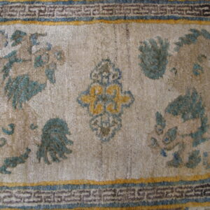 Textured beige rug with faded teal mythological motifs and a detailed blue and yellow geometric border.