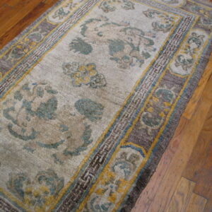 Beige rug with teal and yellow scrolling motifs and complex dark borders on wood floor.