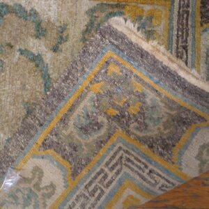 A folded rug corner with geometric patterns in blue, yellow, and brown rests on brown wood flooring.