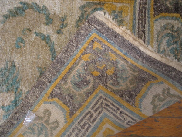 A folded rug corner with geometric patterns in blue, yellow, and brown rests on brown wood flooring.