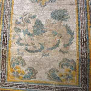 Close-up of a short-pile rug featuring a beige center field, teal and yellow designs, and geometric borders.