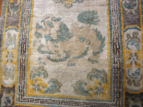 Close-up of a short-pile rug featuring a beige center field, teal and yellow designs, and geometric borders.