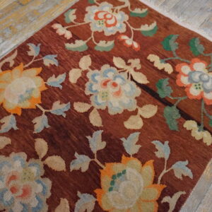 Rust-colored rug with trailing floral designs in cream, blue, and orange sits on distressed wood flooring.