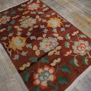 Reddish-brown rug with colorful large floral motifs rests on distressed gray plank wood flooring.