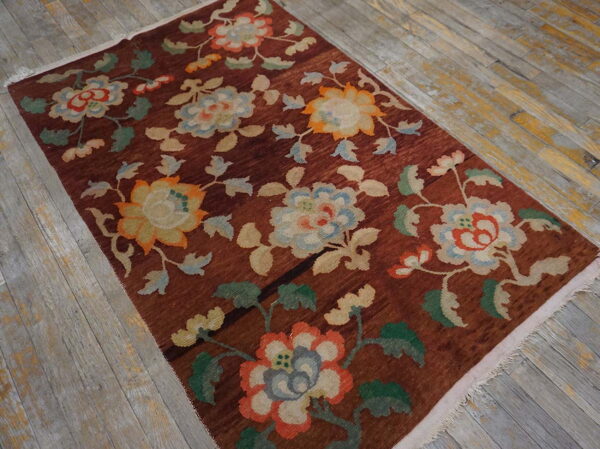 Reddish-brown rug with colorful large floral motifs rests on distressed gray plank wood flooring.