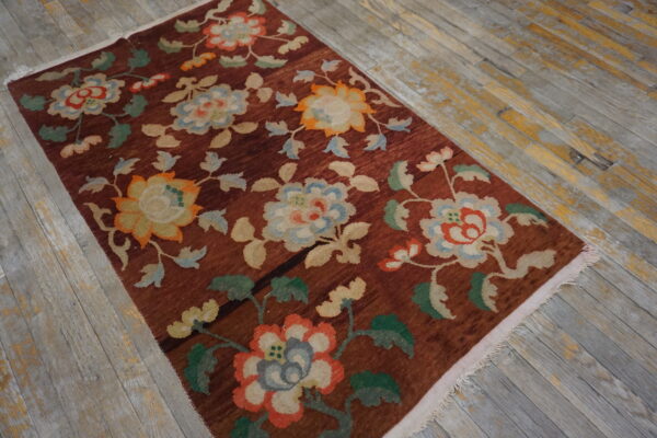 Deep red-brown rug with stylized flowers in blue, green, and orange on weathered wood planks.