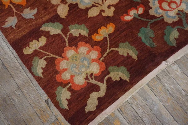 Reddish-brown rug with a dense floral pattern in orange, blue, and green on rustic wood planks.