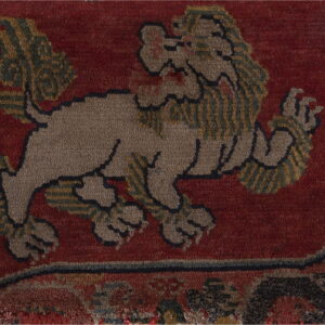 A textured, deep red rug features a central tan and green patterned mythological lion motif.